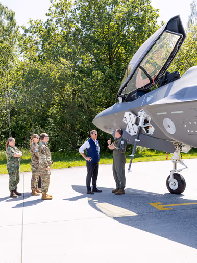 Popolo krijgt naast een F-35 met geopende canopy uitleg van een militair. Op een meter afstand luisteren vier militairen mee.