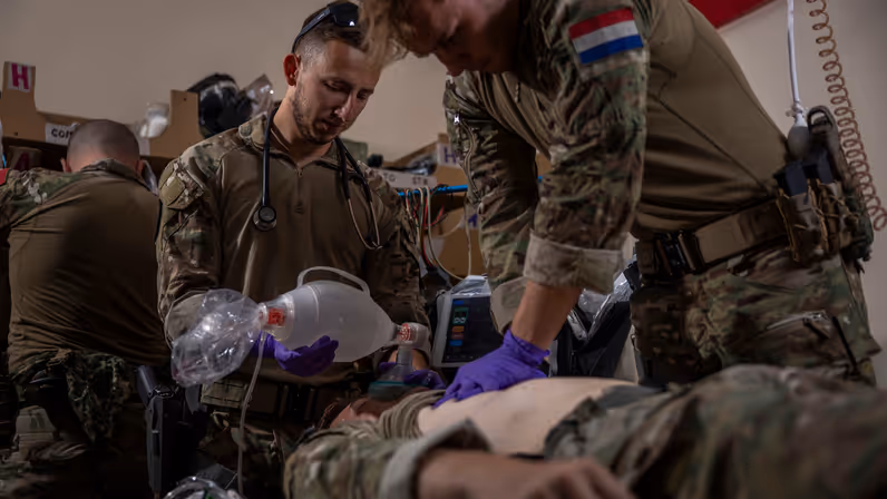 Een militair met een Nederlandse vlag op de schouder reanimeert een pop. Een collega geeft het gefingeerde slachtoffer zuurstof met een rubberen knijpzak.  