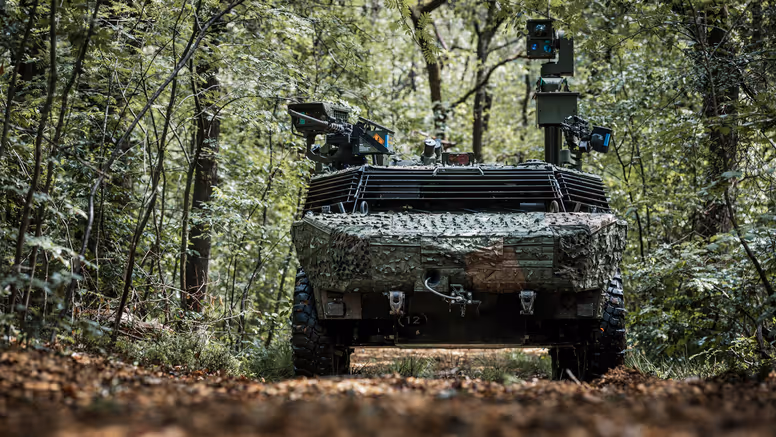 Militair voertuig dat gecamoufleerd door een bos rijdt.