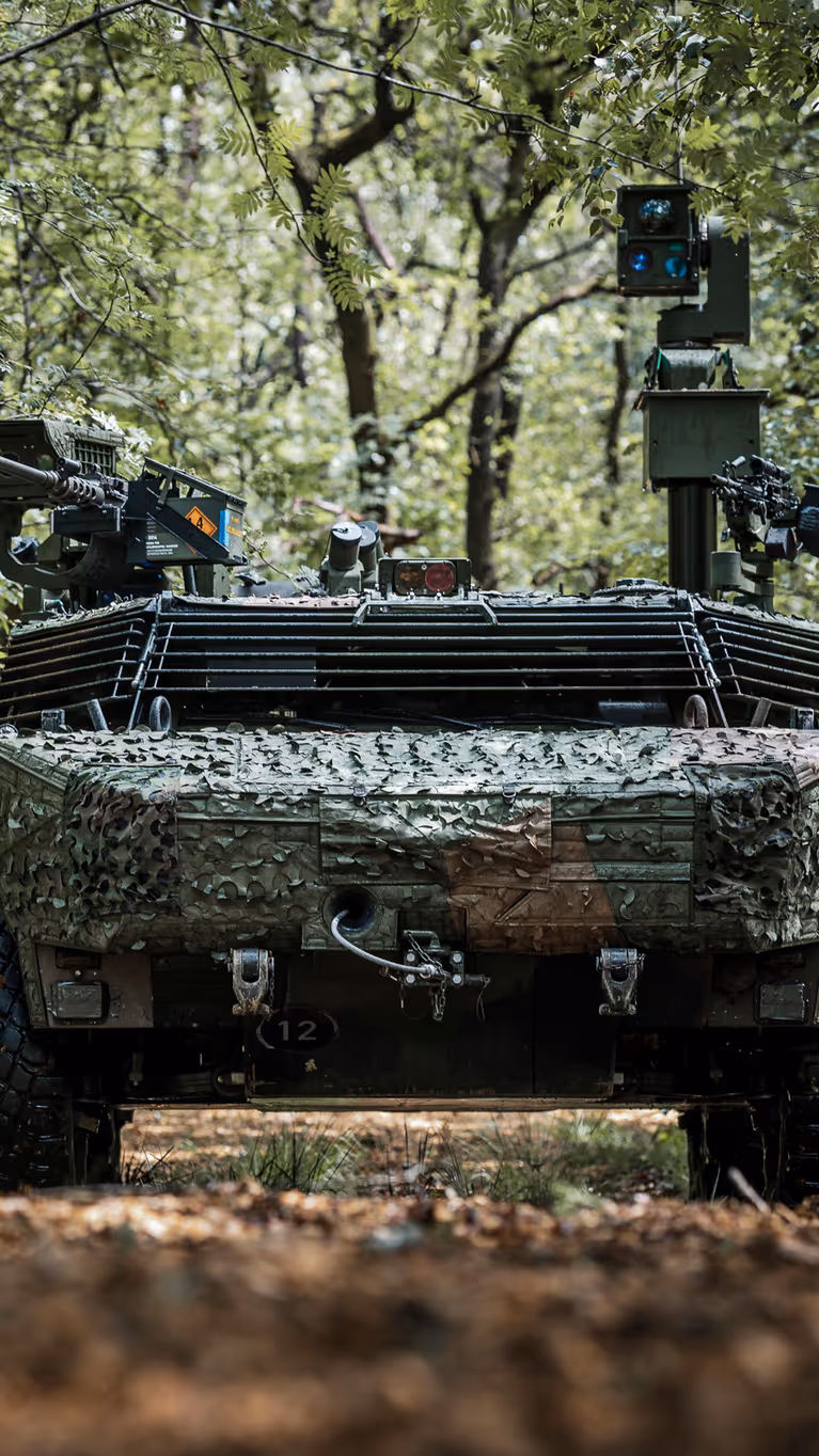 Militair voertuig dat gecamoufleerd door een bos rijdt.