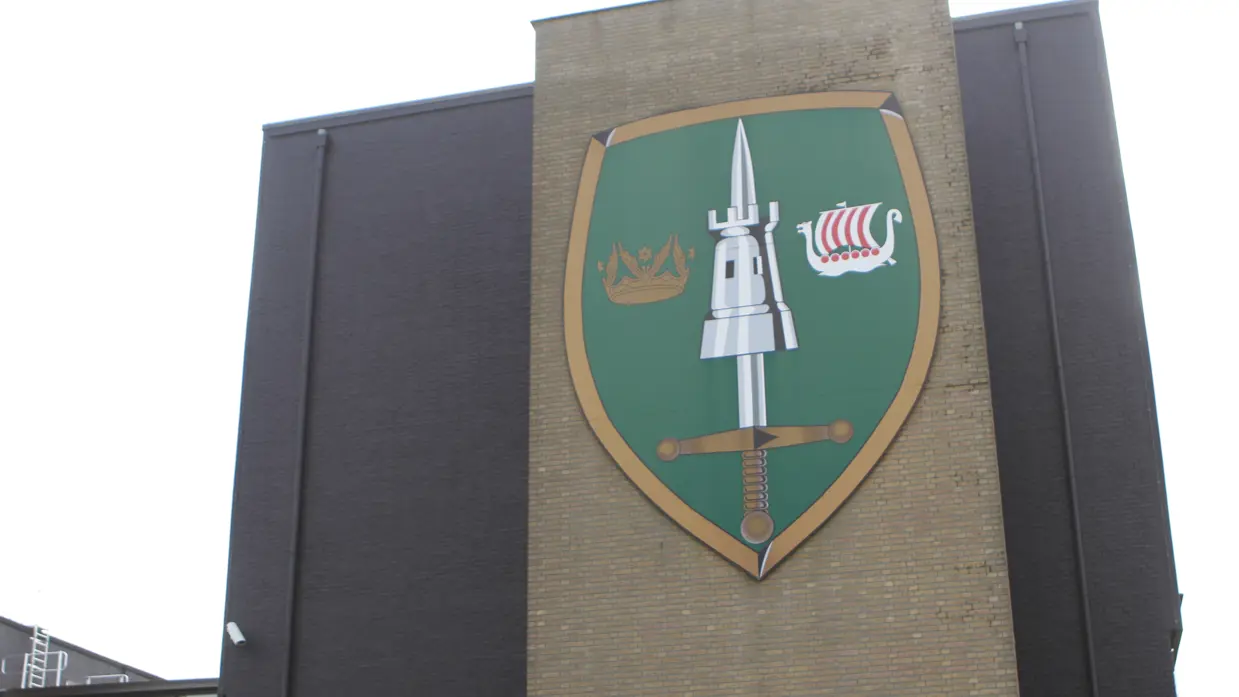 Het wapenembleem van het JFC, groot afgebeeld op een gevel.