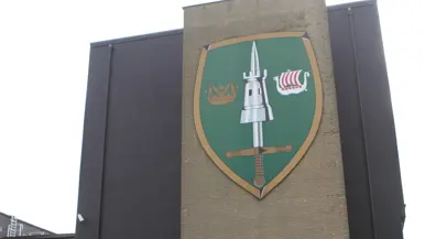 Het wapenembleem van het JFC, groot afgebeeld op een gevel.
