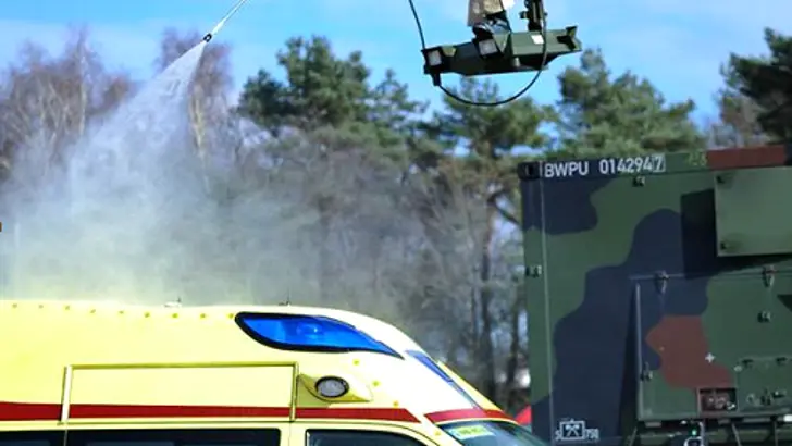 Persoon in beschermend pak spuit vanaf een kraan een ambulance schoon.