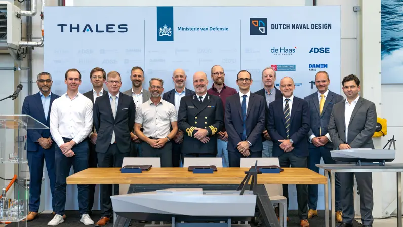 Een grote groep mannen in pak en uniform voor een groot bord met namen van bedrijven.