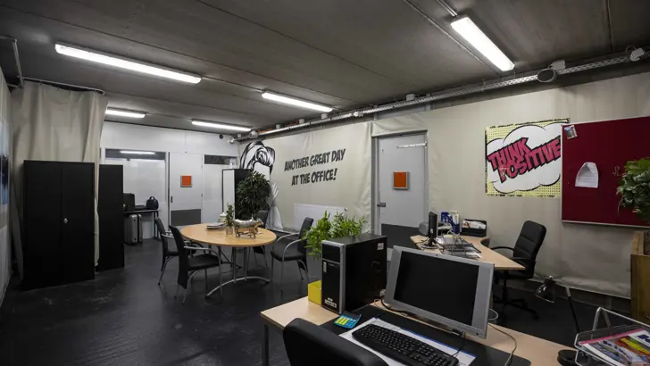 Kantoorruimte met onder meer bureaus, vergadertafel, kasten en computers.