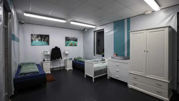 Slaapkamer met 2 bedden, een kinderbedje, nachtkastjes, lampen en een kledingkast.