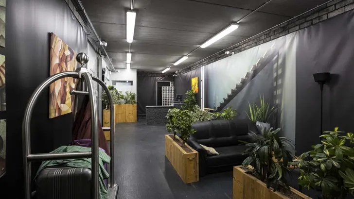 Hotellobby met plantenbakken, koffers en zitgedeelte.