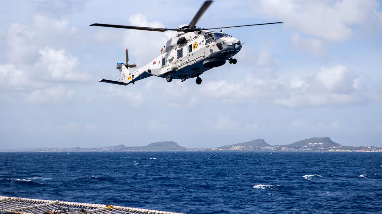 Helikopter boven zee met land in zicht.