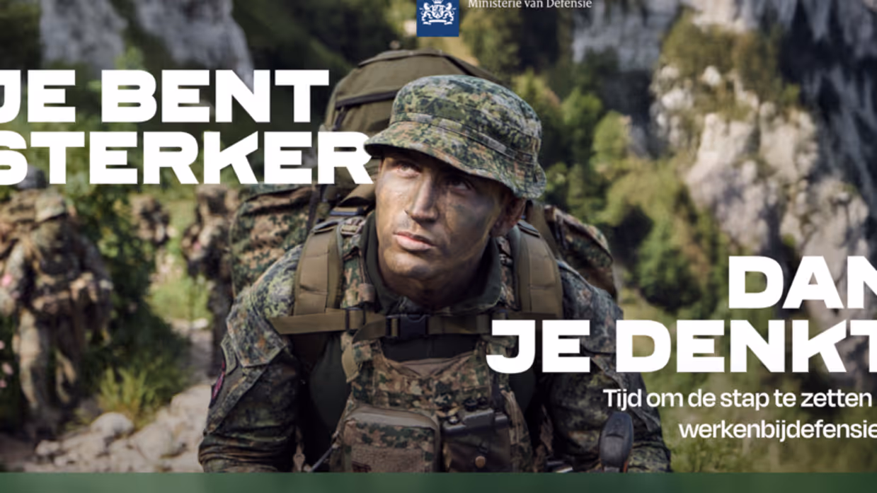 Militair in uniform met groengekleurd gezicht en een slap hoedje op. Op zijn rug een rugzak. Rotsige bergen op de achtergrond.