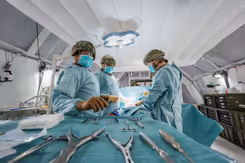 Leden van een chirurgisch team met helmen op en groene pakken aan. Op de voorgrond zilverkleurig medisch gereedschap.