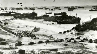 De geallieerde vloot landt in Normandië met assistentie van vele schepen van de koopvaardij en koopvaardijschepen liggen aangemeerd aan een van de pontons van de kunstmatige Mulberry-haven in Arromanches-les-Bains.