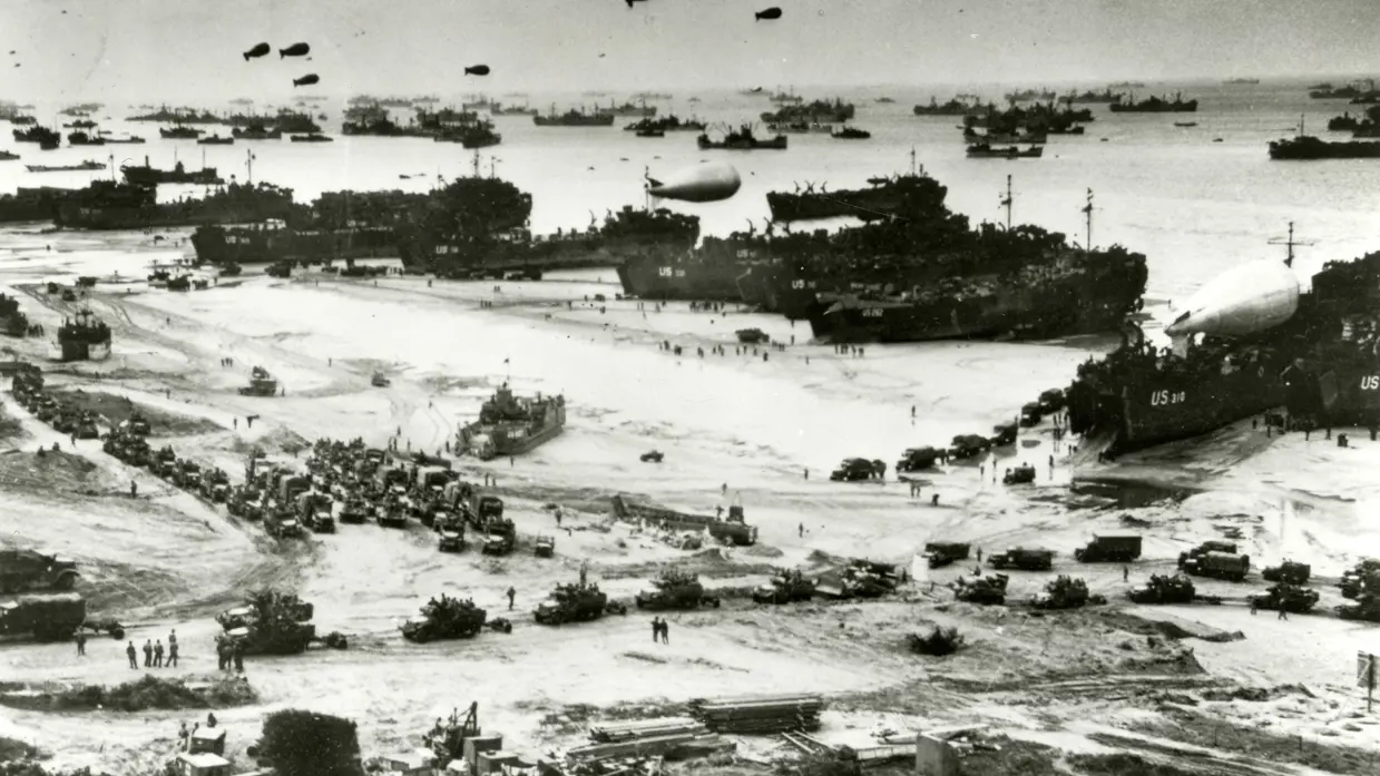 De geallieerde vloot landt in Normandië met assistentie van vele schepen van de koopvaardij en koopvaardijschepen liggen aangemeerd aan een van de pontons van de kunstmatige Mulberry-haven in Arromanches-les-Bains.