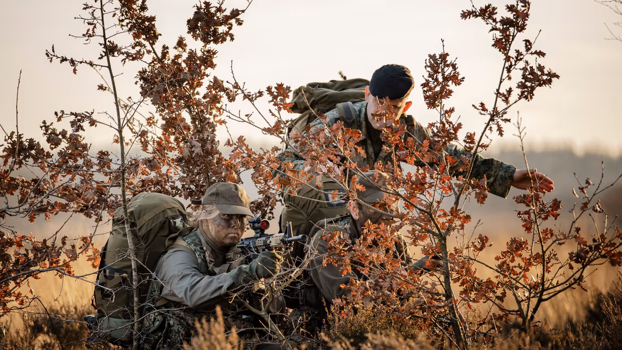 Amalia zit gecamoufleerd tussen de struiken met een geweer en haar rangonderscheidingstekens worden gedoopt.