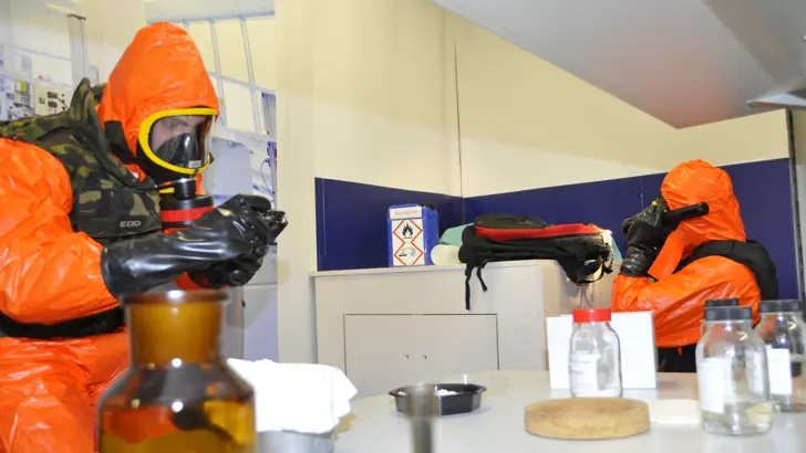 Personen in beschermende oranje pakken doen een analyse in een lab.