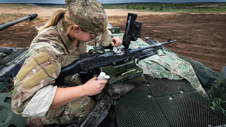 Vrouwelijke militair in een tank controleert geweer.