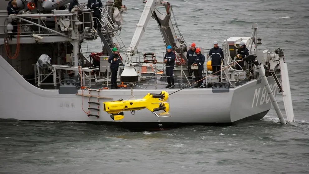 Marineschip waarop militairen een gele onderwaterrobot te water laten.