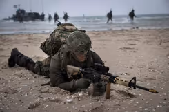 Militair ligt tijdens oefening met wapen gericht op zijn buik op een strand.