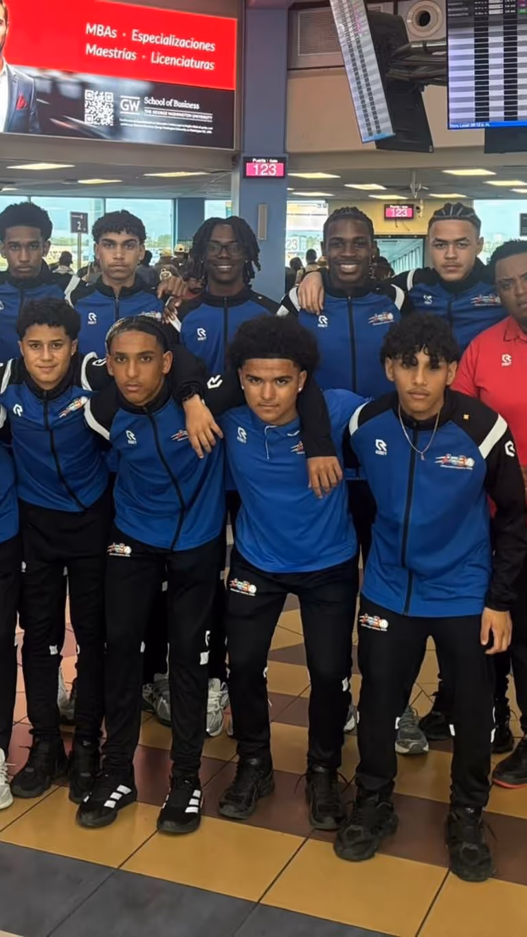 Een elftalfoto met spelers, trainers en coaches op de luchthaven. 