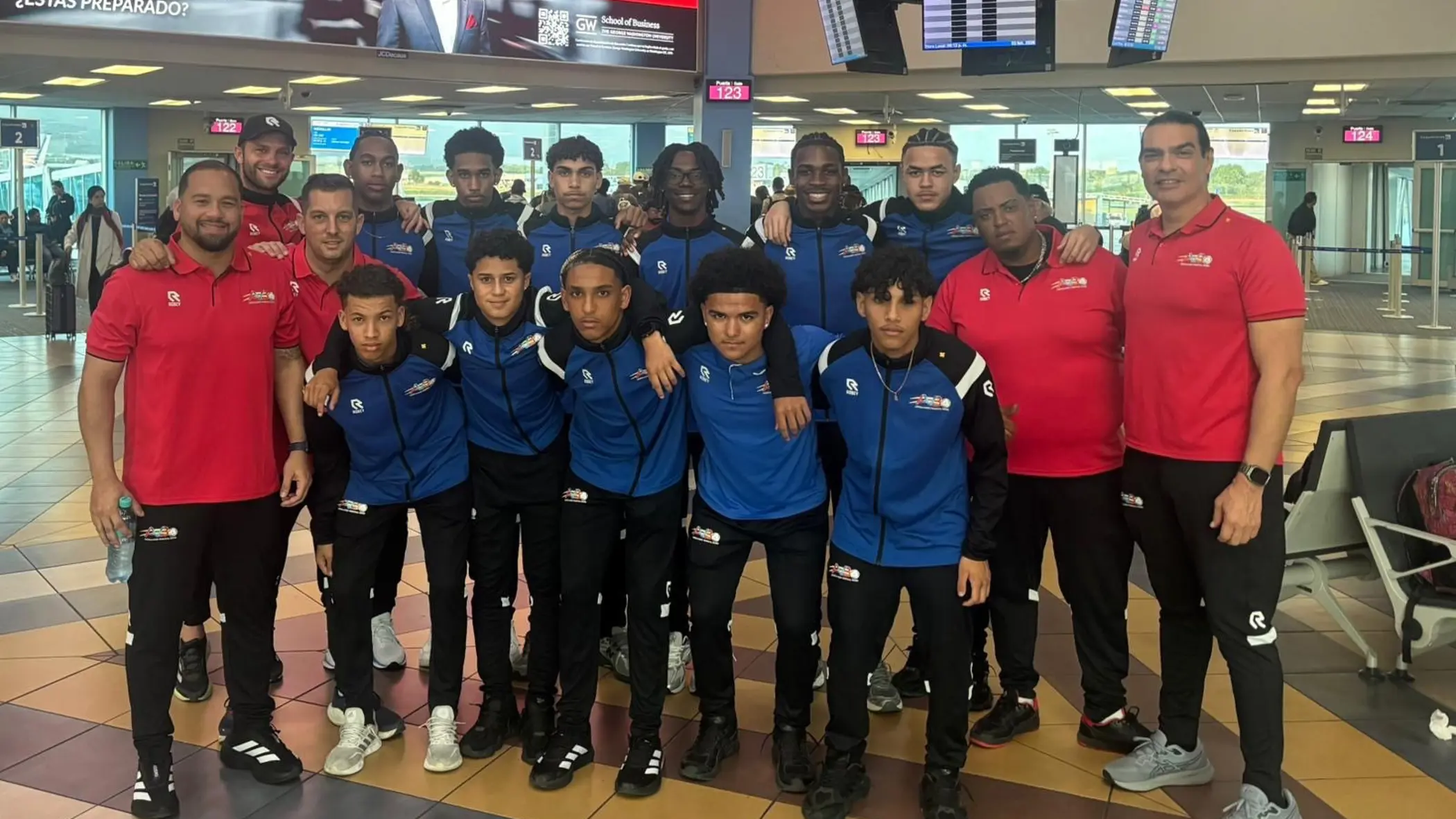 Een elftalfoto met spelers, trainers en coaches op de luchthaven. 