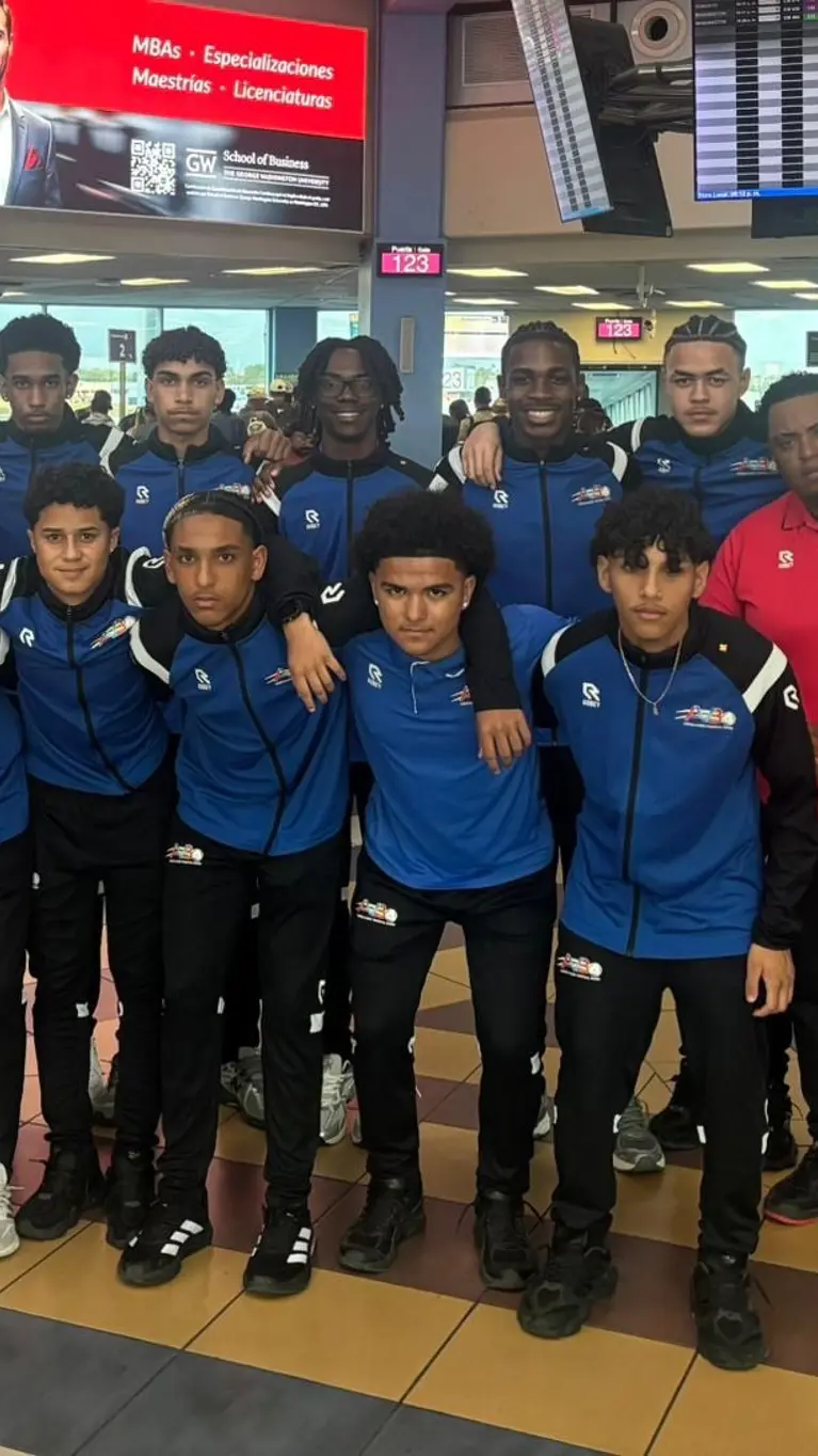 Een elftalfoto met spelers, trainers en coaches op de luchthaven. 
