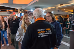 2 bezoekers luisteren naar een defensiemedewerker.