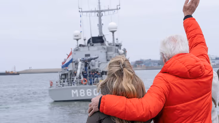 Een man en een vrouw op de kade zwaaien naar de bemanning op het schip. 