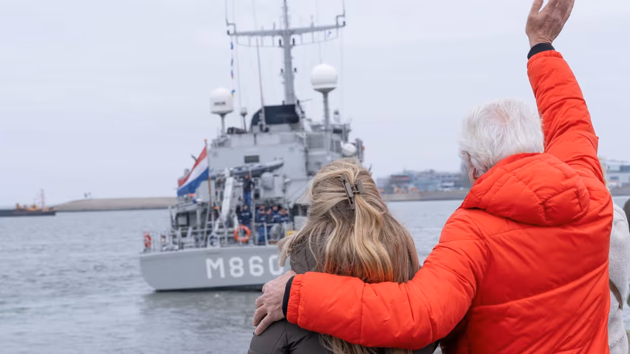 Een man en een vrouw op de kade zwaaien naar de bemanning op het schip. 