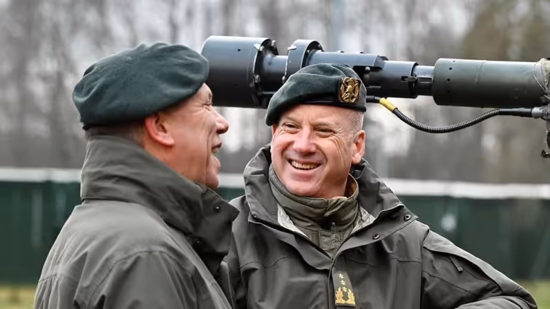 Twee militairen, lachend in gesprek met elkaar. Op de achtergrond de loop van een kanon.
