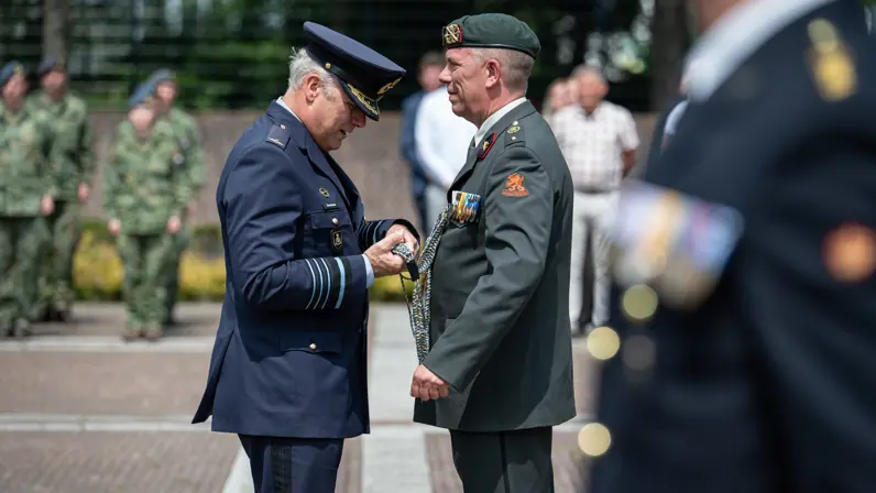 Commandant der Strijdkrachten tegenover adjudant Cees Bielander op een plein met daar omheen militairen en burgers die toekijken.