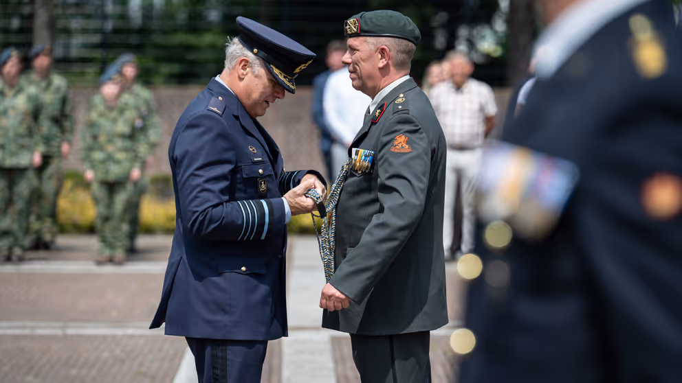 Een militair hangt een andere militair iets om.