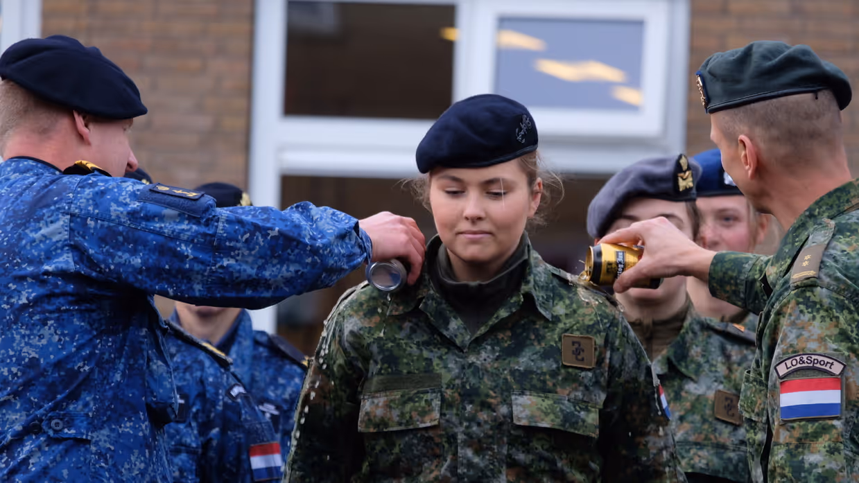 Twee militairen gieten bier over de rangonderscheidingstekens op de schouders van Prinses Amalia.