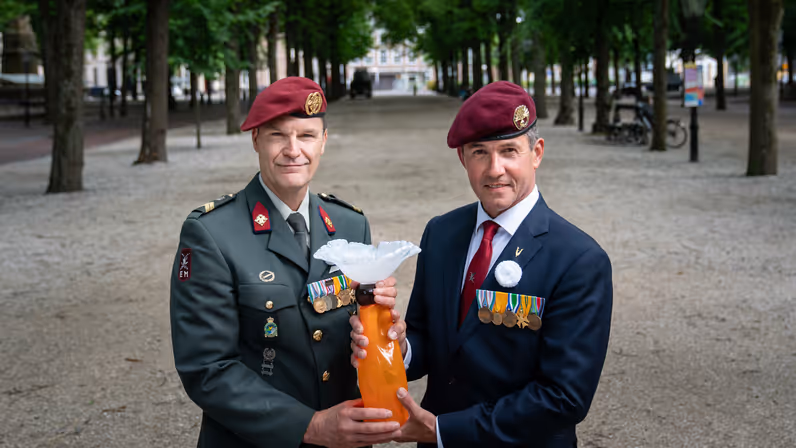Twee militairen houden een beeld van een witte anjer vast. 