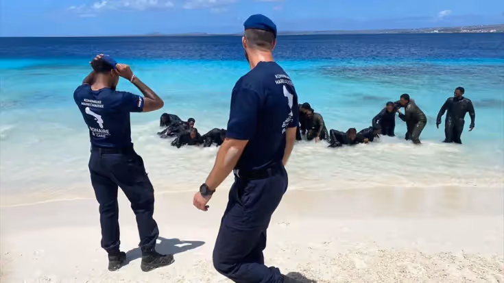 Aspiranten liggen in zee, instructeurs kijken toe vanaf het strand.