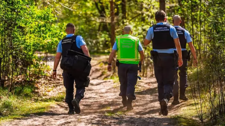 Vier marechaussees op de rug gezien, lopen door de natuur.