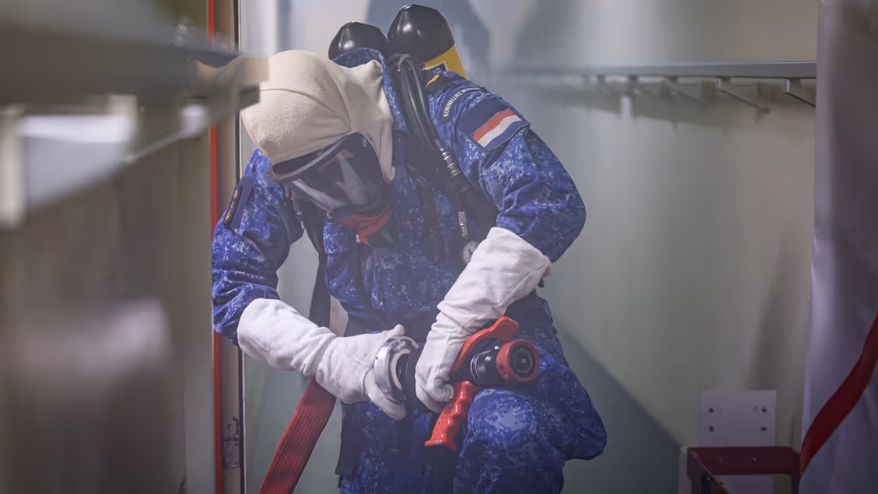 Een marineman draagt een persluchtmasker en in omgeven door rook aan boord.