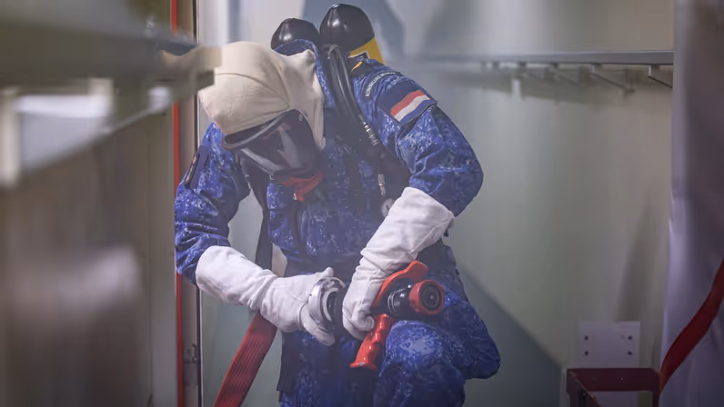 Een marineman draagt een persluchtmasker en in omgeven door rook aan boord.
