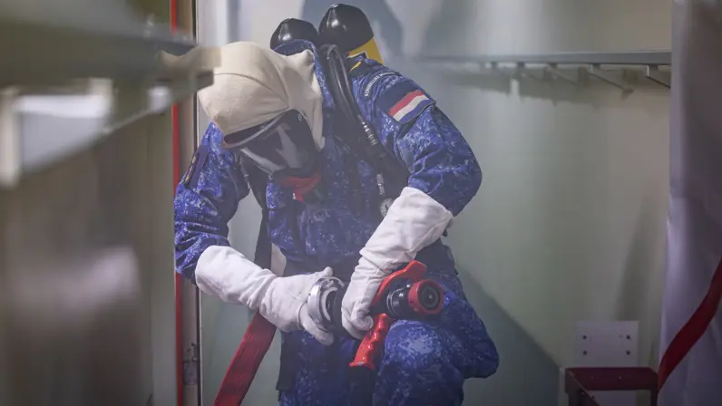 Een marineman draagt een persluchtmasker en in omgeven door rook aan boord.