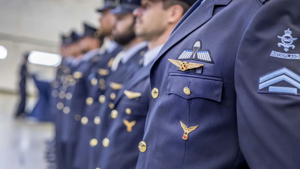Een rij militairen in dagelijks tenue onscherp in beeld. Op de borst van de eerste militair prijkt de wing.