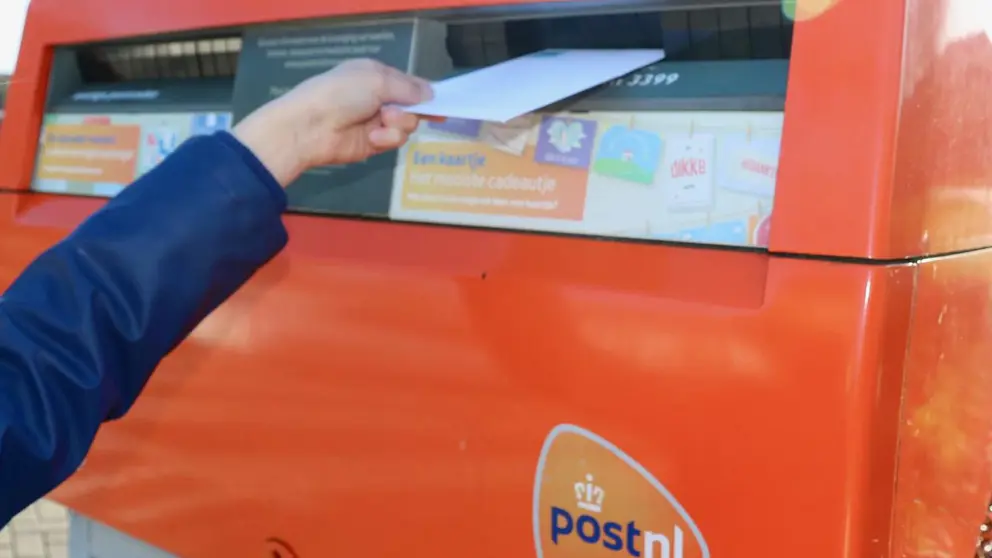 Iemand stopt een brief in een brievenbus.