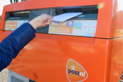 Iemand stopt een brief in een brievenbus.