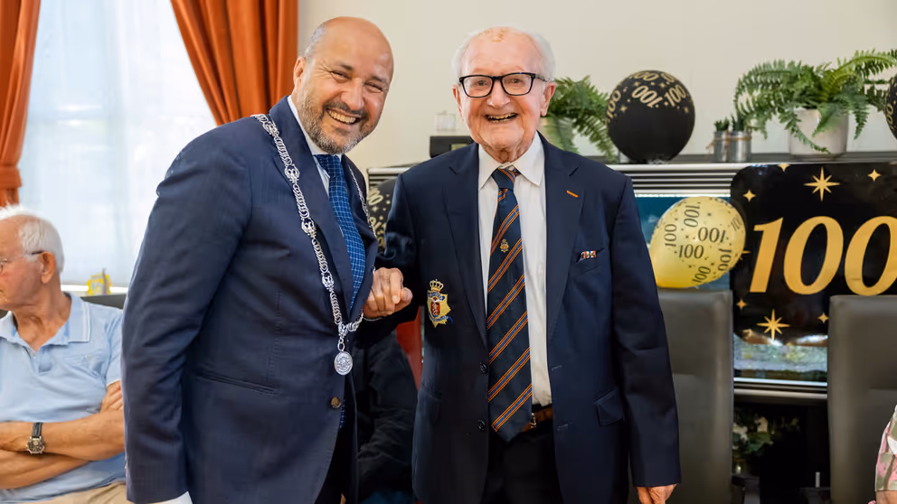 Burgmeester met ambtsketen staat naast 100-jarige veteraan.