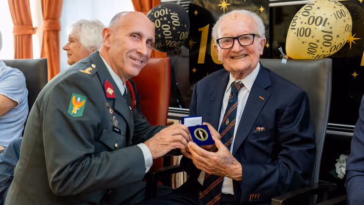 Commandant reikt 100-jarige coin uit.