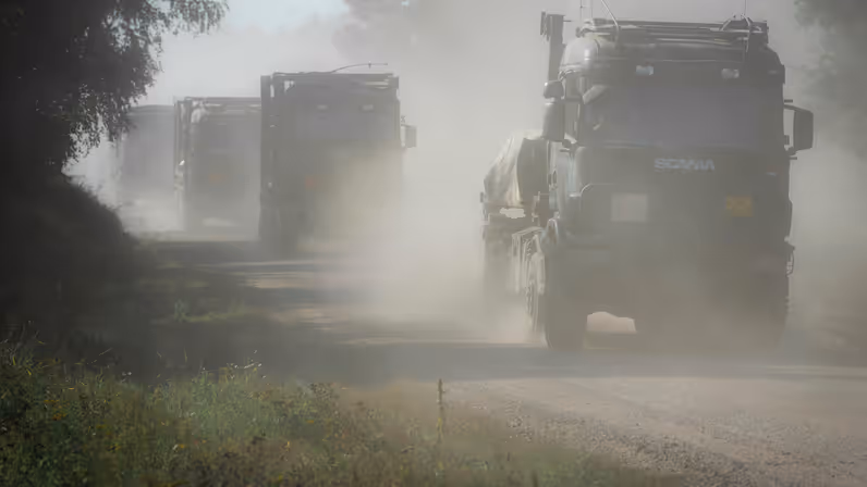 Militaire vrachtwagens rijden over een stoffig pad