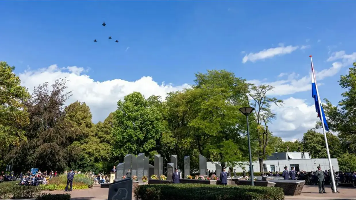 Vijf F-35’s vliegen in Missing Man-formatie boven het Nationaal Herdenkingspark in Roermond. Militairen en burgerpubliek staan op de grond.