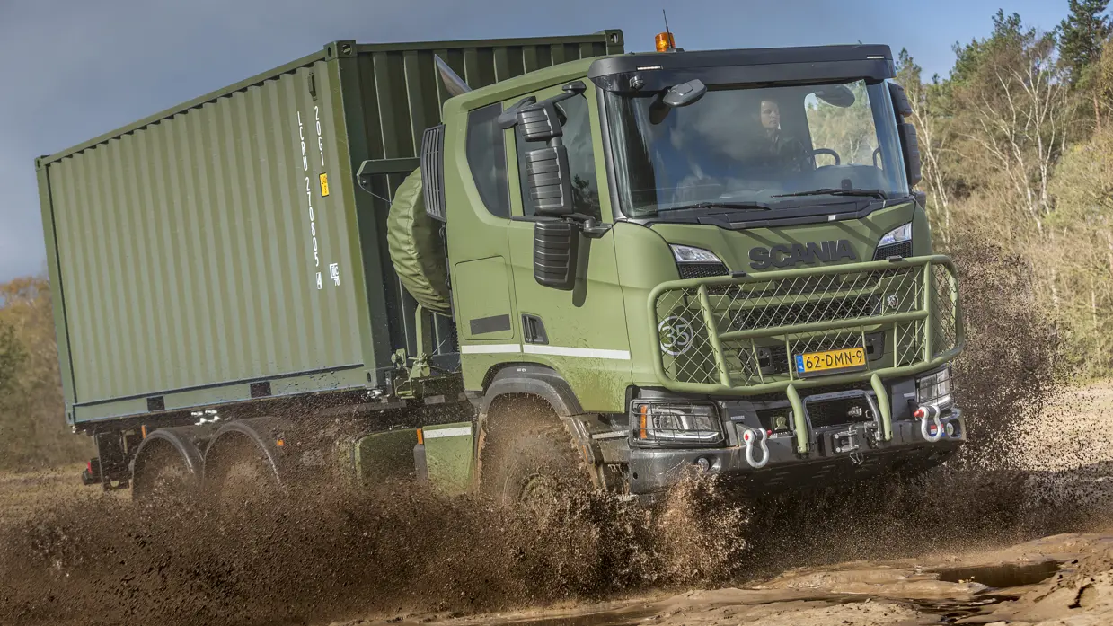 Opspattende modder rond een gloednieuwe, 3-assige Scania Gryphus die op een oefening terrein door plassen rijdt.