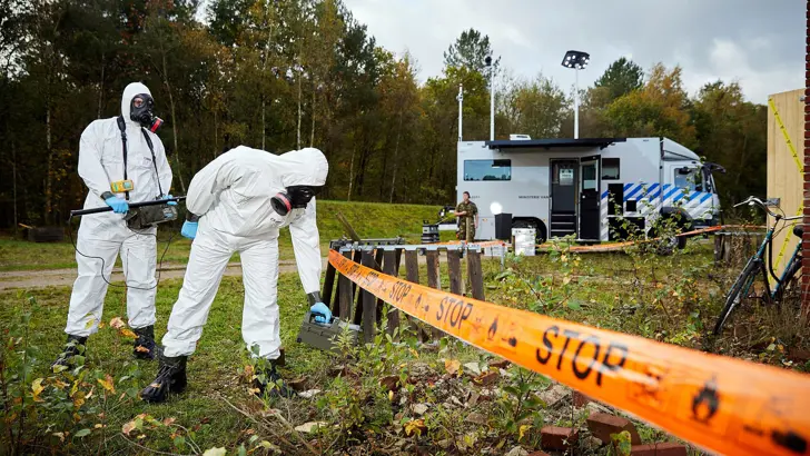 2 personen in beschermende pakken voeren een meting uit op een veld.