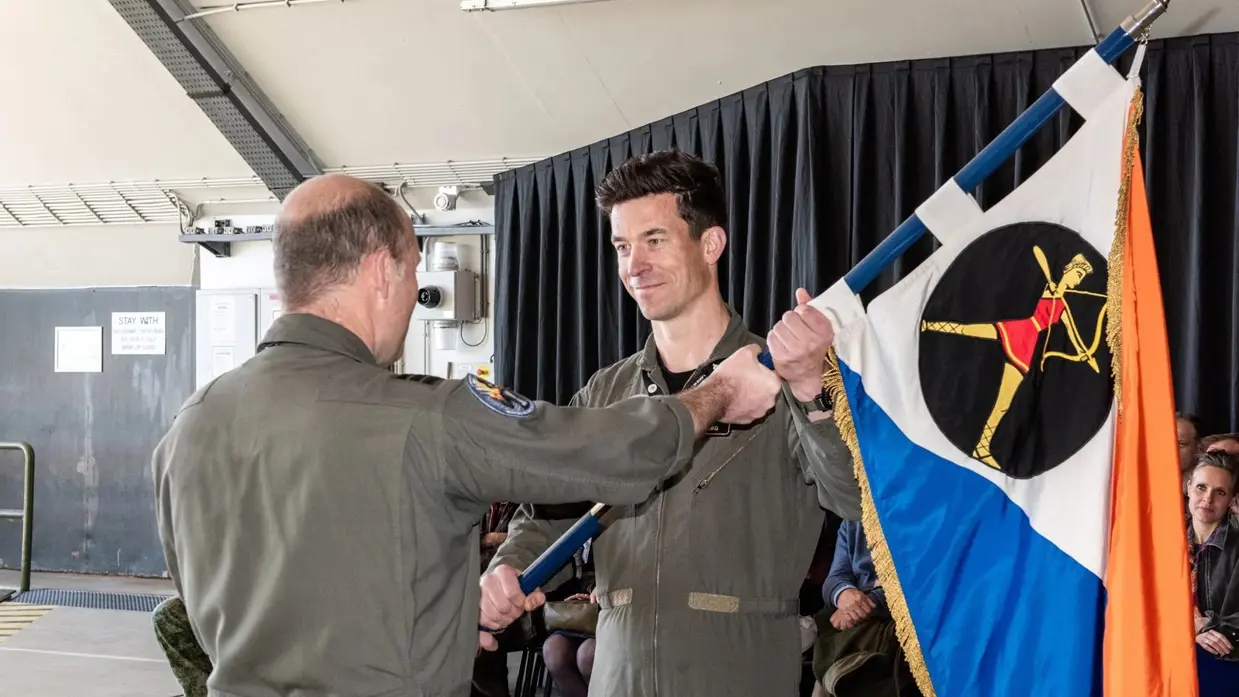 Scherders neemt de squadronvlag in ontvangst uit handen van Van de Graaf. Achter hen zit publiek.