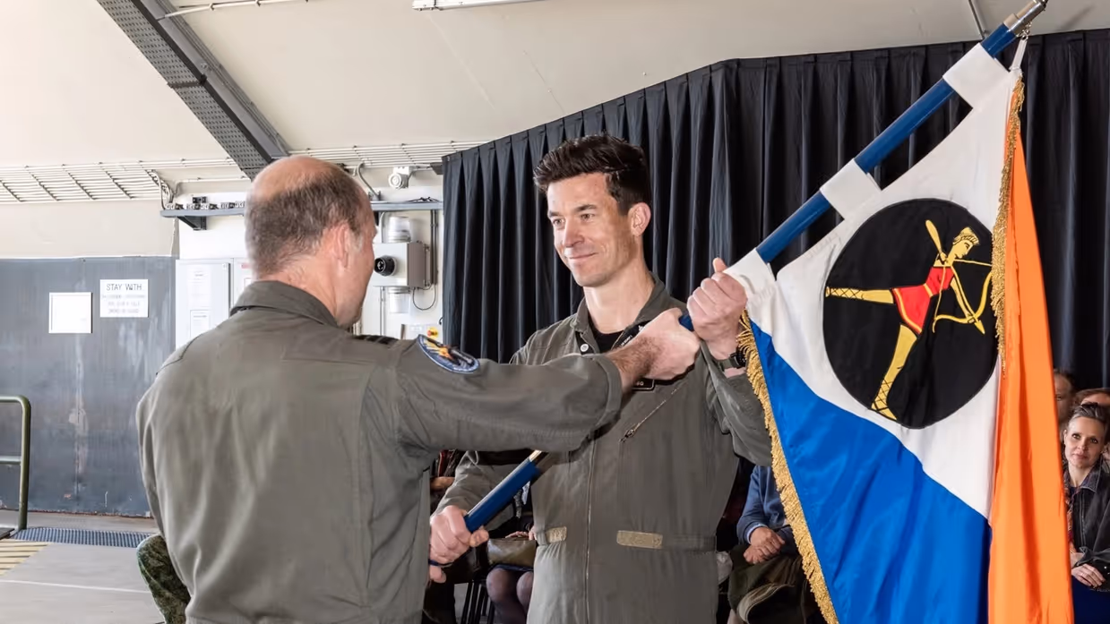 Scherders neemt de squadronvlag in ontvangst uit handen van Van de Graaf. Achter hen zit publiek.