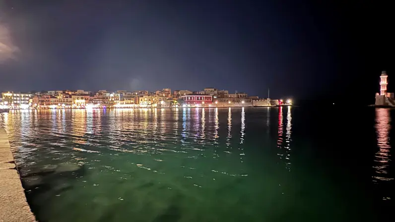 Avondfoto van de lichtjes van de stad Chania die weerspiegelen in het zeewater.