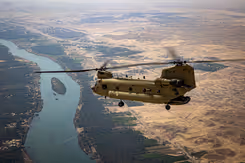 Chinook-transporthelikopter boven een meanderende rivier en woestijngebied.